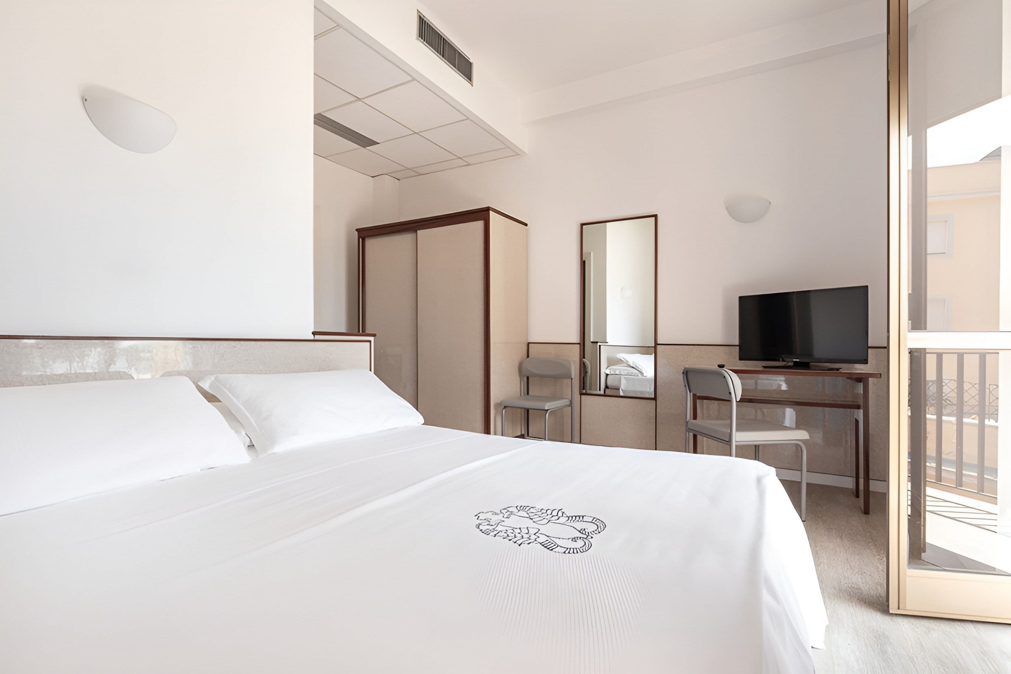Quarto de hotel com cama, escrivaninha, televisão, cadeira e varanda.