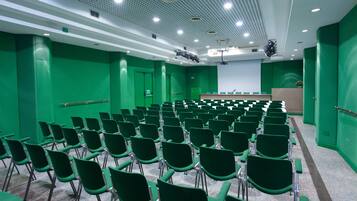 A conference room with rows of green chairs, a podium, and a projector screen.