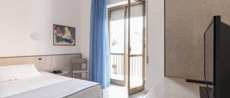 Een hotelkamer met een bed, een bureau, een stoel, een televisie en een schuifdeur naar een buitenruimte.