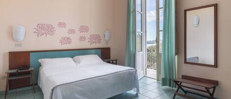 A hotel room with a bed, bedside tables, a bench, a wall-mounted light, and a window with curtains.