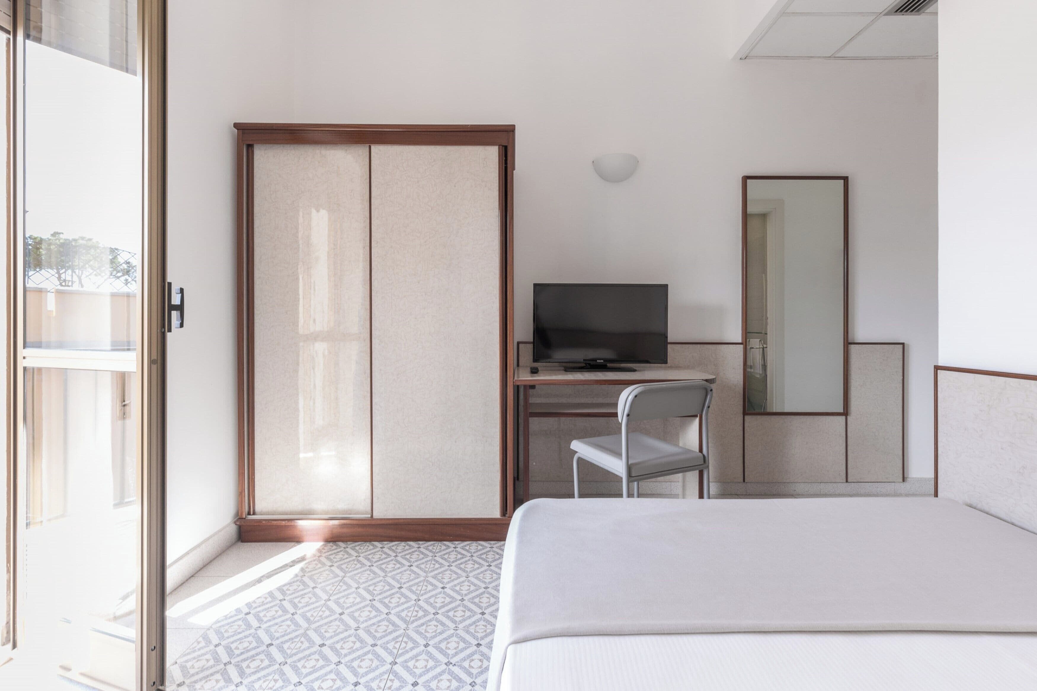 Habitación de hotel con cama, escritorio con televisor, silla, armario y espejo grande.