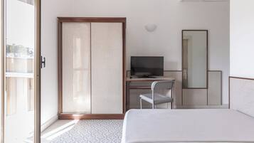 Une chambre d’hôtel comprenant un lit, un bureau avec une télévision, une chaise, une armoire et un grand miroir.
