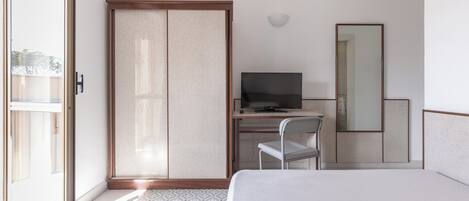 Habitación de hotel con cama, escritorio con televisor, silla, armario y espejo grande.