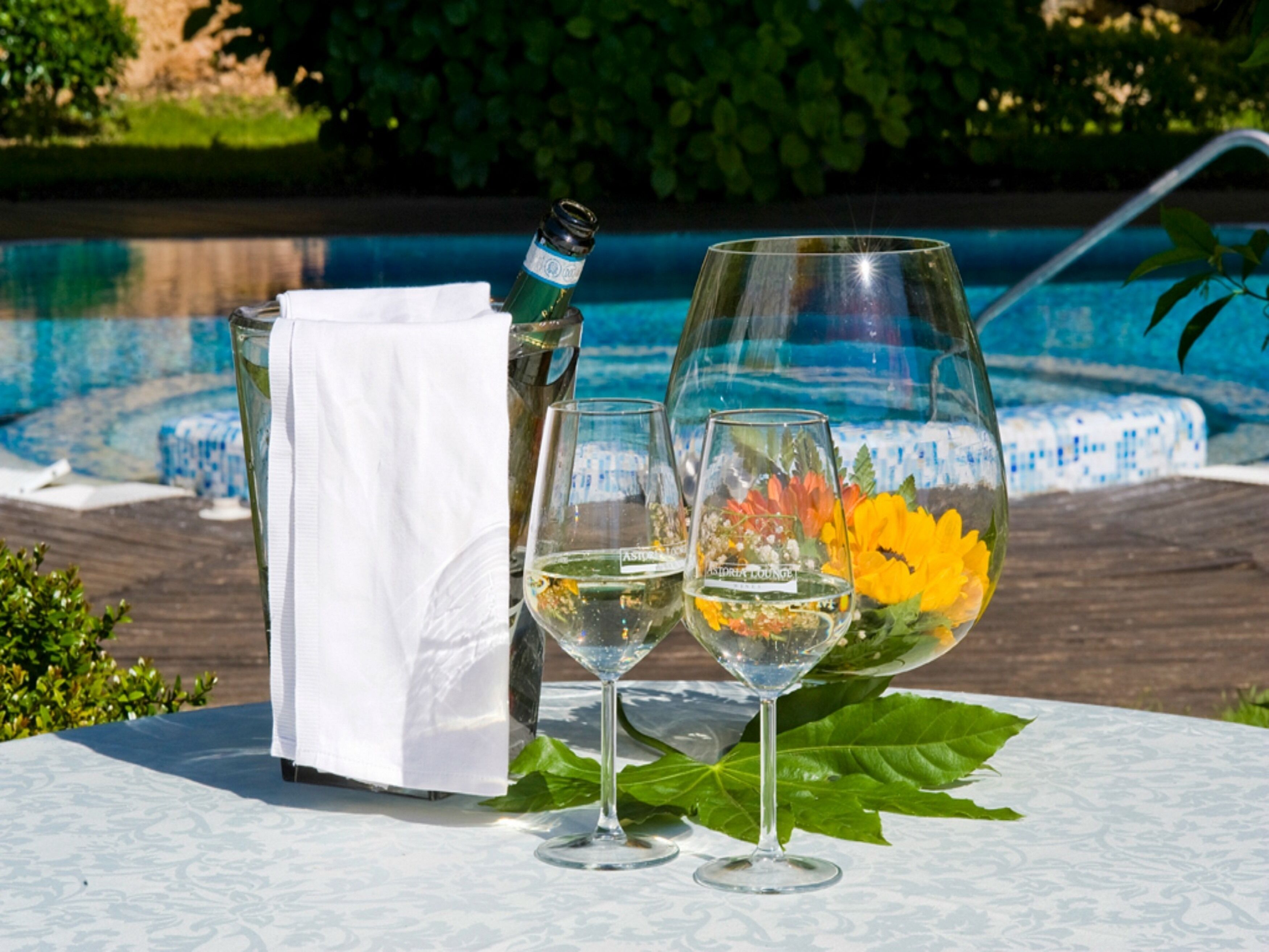 Uma mesa com duas taças de vinho, uma garrafa e um guardanapo perto de uma piscina.