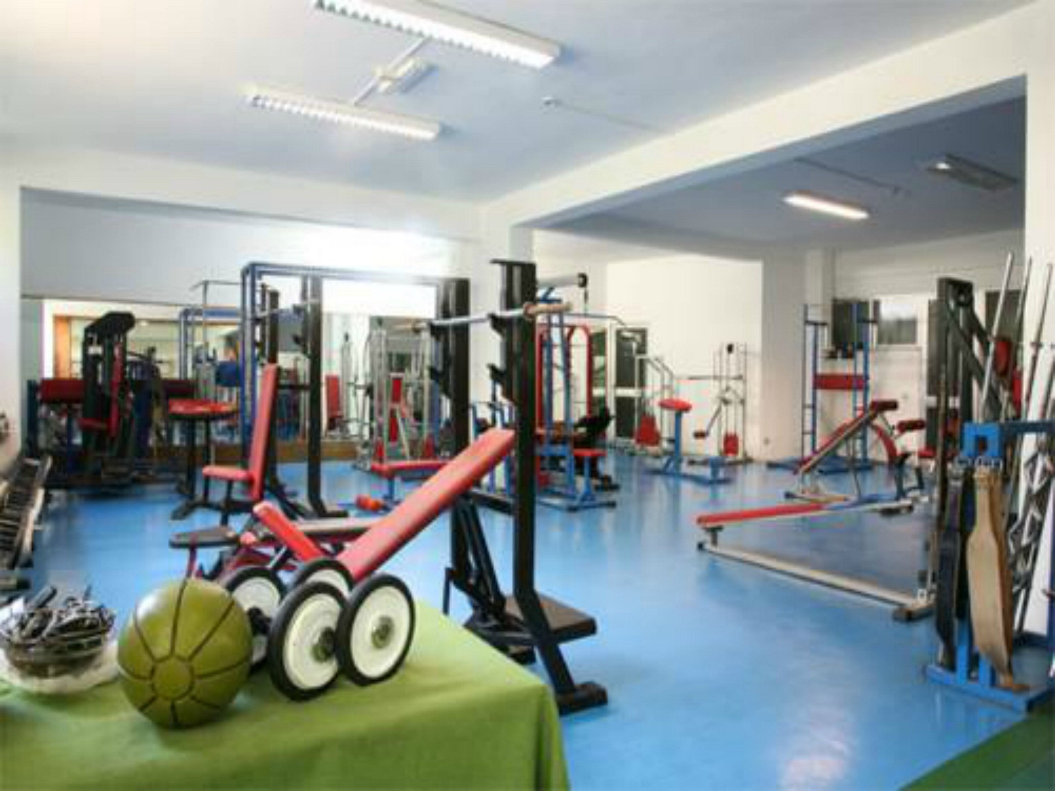 A gym with various exercise equipment, a green table with sports balls, and a blue floor.