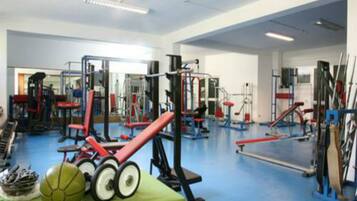 Un gimnasio con diferentes máquinas de ejercicio, una mesa verde con balones deportivos y un suelo azul.