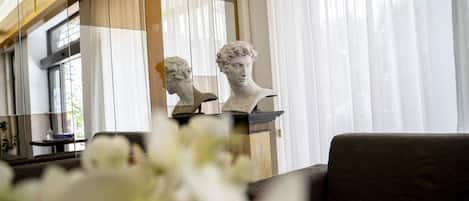A room with a sofa, a bust sculpture, and a window with sheer curtains.