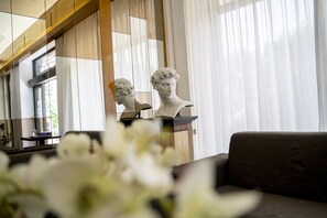 A room with a sofa, a bust sculpture, and a window with sheer curtains. - Hotel Dei Fiori (Milan)