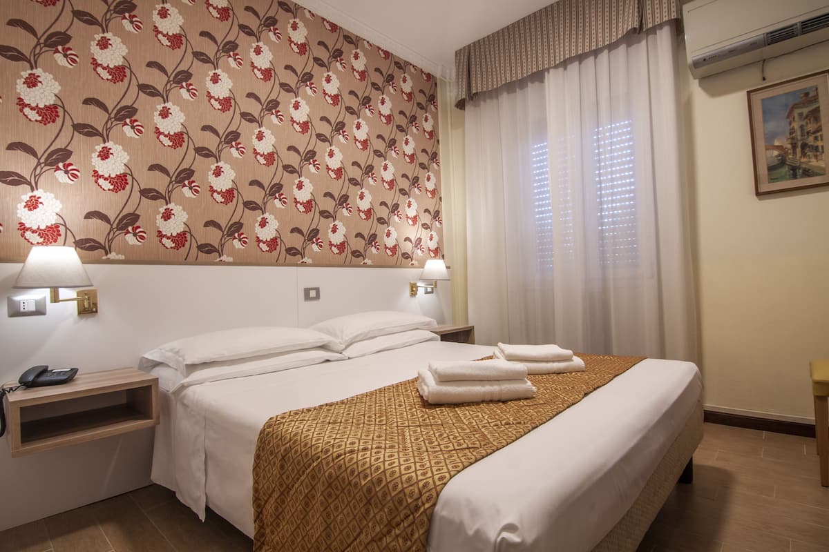 Ett hotellrum med en stor säng, två sängbord, en telefon som sitter fast på väggen och ett fönster med gardiner.