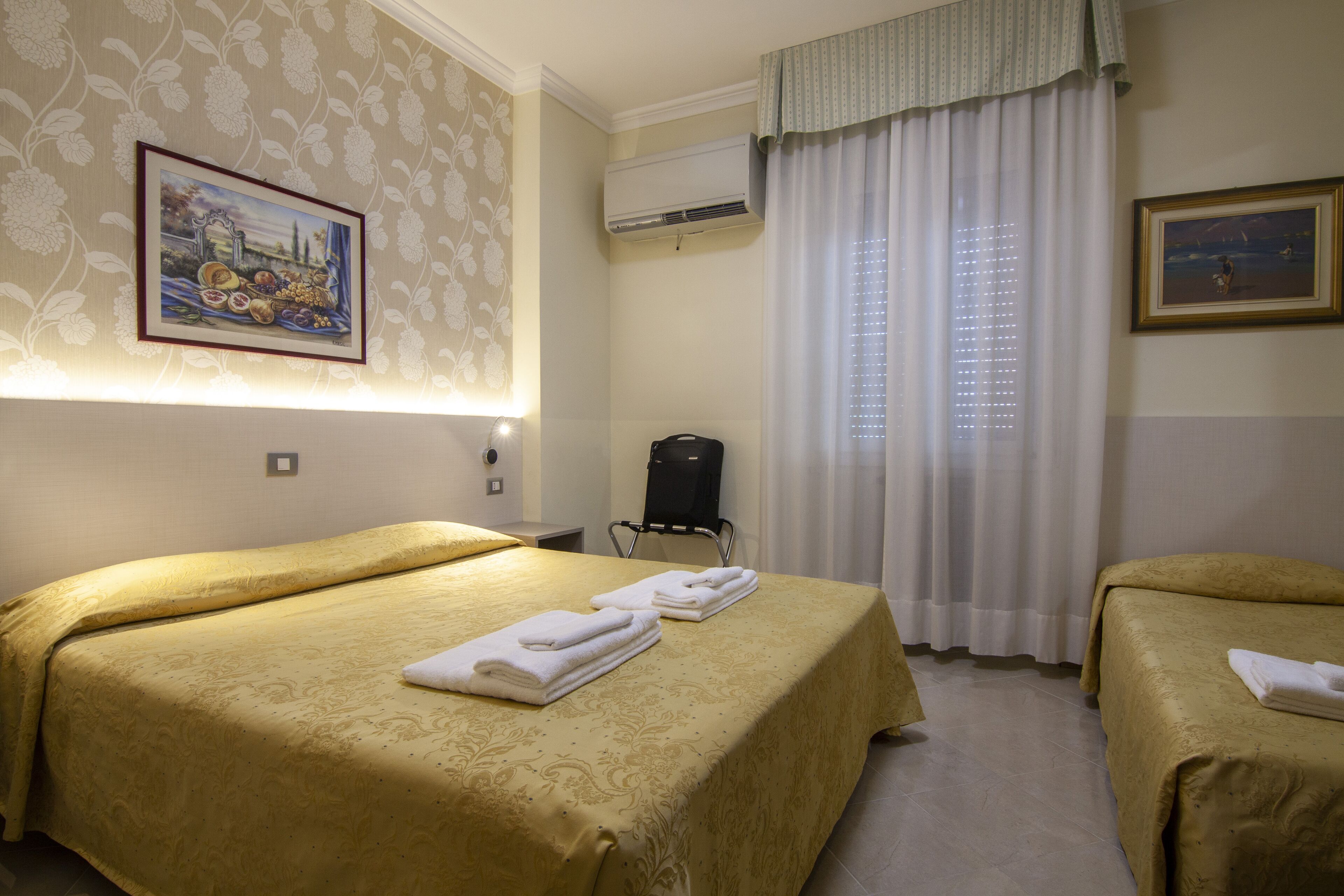 A hotel room with two beds, a painting on the wall, an air conditioning unit, and a window with curtains.