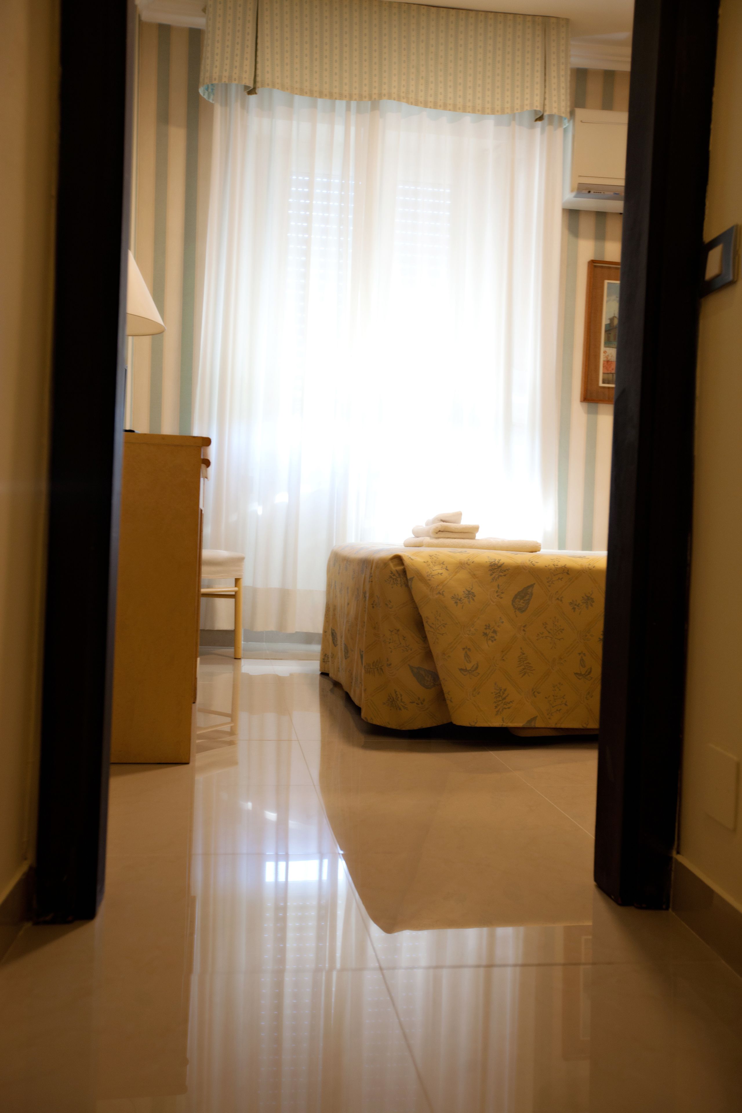 Quarto de hotel com cama, uma cadeira, escrivaninha e janela com cortinas.