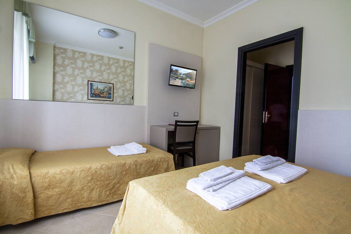 Ett hotellrum med två separata sängar, ett skrivbord, en stol, en tv och en dörr.