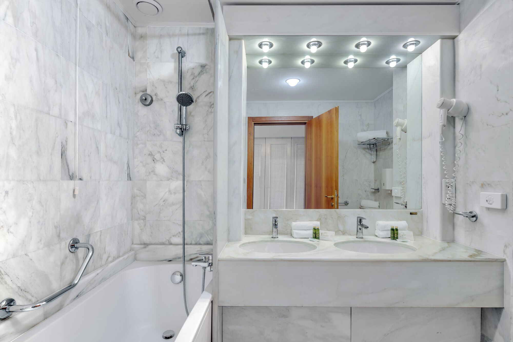 Ein modernes Badezimmer mit einer Badewanne, zwei Waschbecken und einem großen Spiegel mit Beleuchtung darüber.