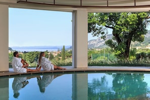 A couple sitting by a pool with a view of a lake and mountains. - Poiano Garda Resort Hotel (Garda)