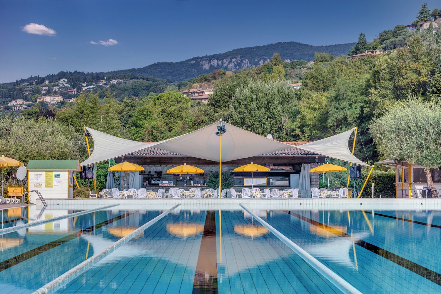 Una piscina con sombrillas, sillas de descanso y vistas a una colina con edificios.