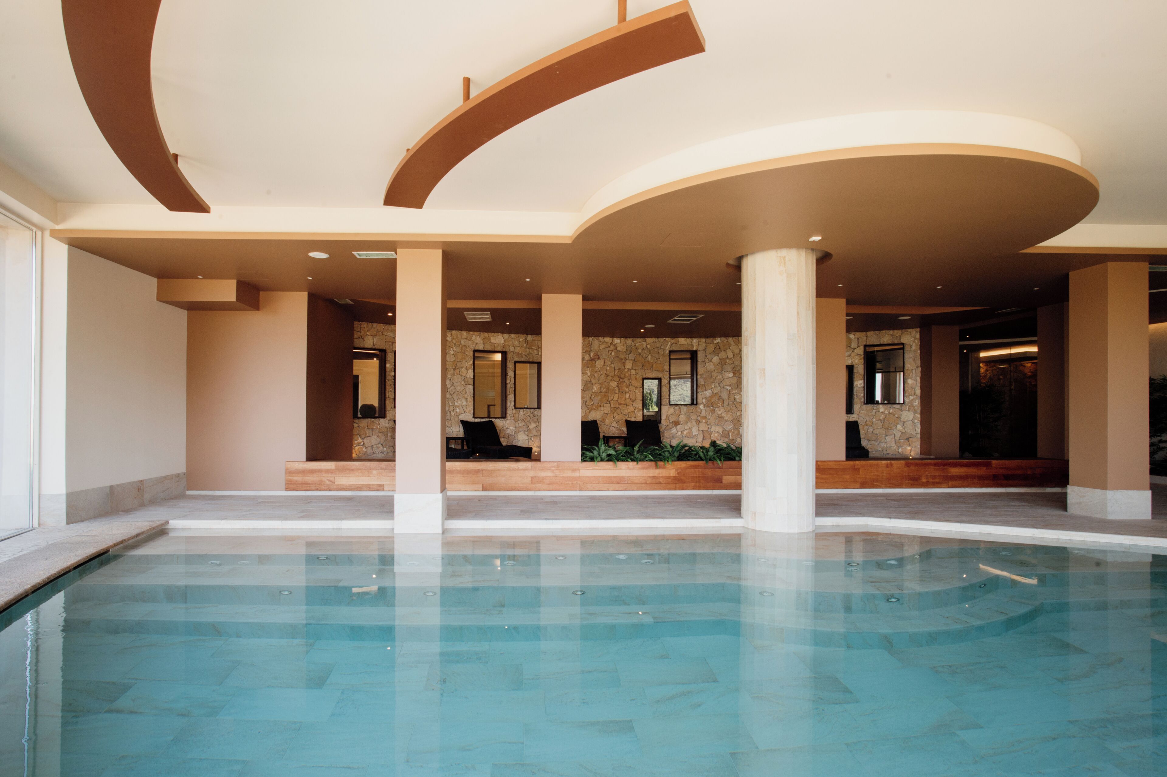 Una amplia piscina interior con un diseño moderno, rodeada de muros y columnas de piedra.