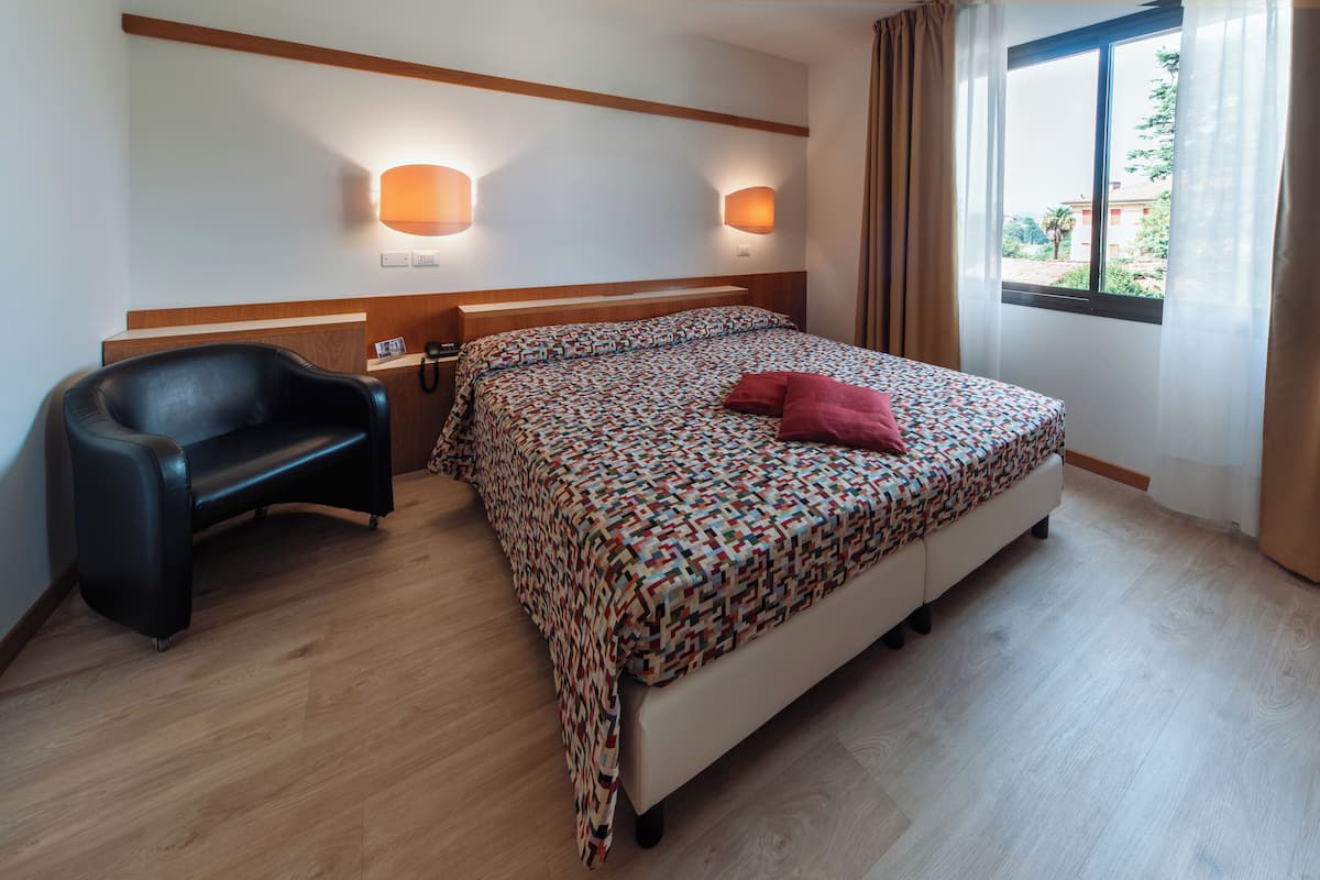 A hotel room with a bed, a chair, a desk, and a window with curtains.