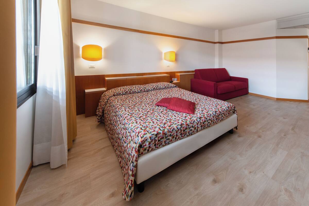 A bedroom with a bed, a red chair, and two wall-mounted lamps.