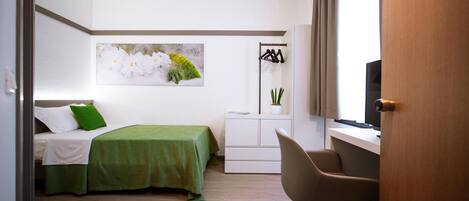 A bedroom with a bed, a desk, a chair, a television, and a wall-mounted plant.