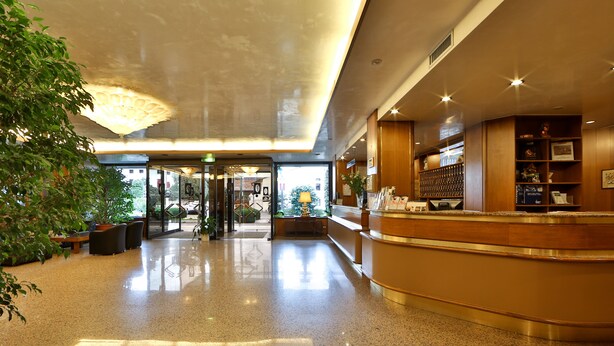 A hotel lobby with a polished floor, a reception desk, and a large potted plant.