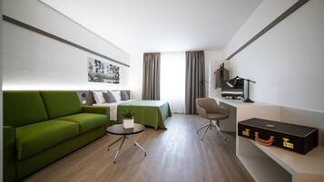 Een moderne hotelkamer met een groene bank, een bed, een bureau met een lamp en een koffer.