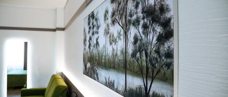 A modern room with a large painting of a forest scene on the wall, a green sofa, and a window providing natural light.