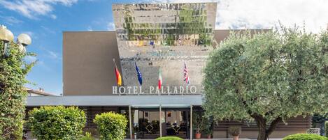 A hotel entrance with a modern facade, flags, and well-maintained landscaping.
