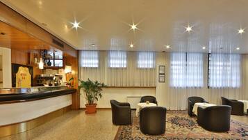 A hotel lobby with a reception desk, seating area, and large windows with curtains.