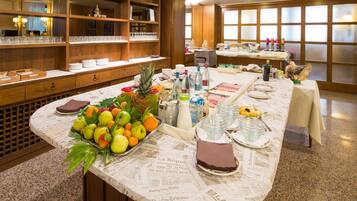 A buffet setup with a variety of fruits, beverages, and dishes on a table covered with newspaper.