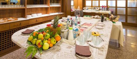 A buffet setup with a variety of fruits, beverages, and dishes on a table covered with newspaper.
