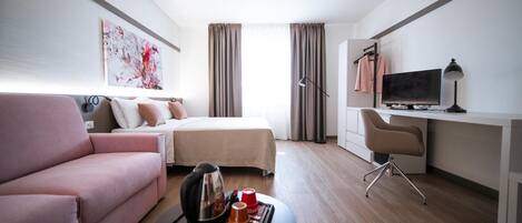 A hotel room with a bed, a desk with a TV, a chair, a coffee table with a tray, and a pink sofa.