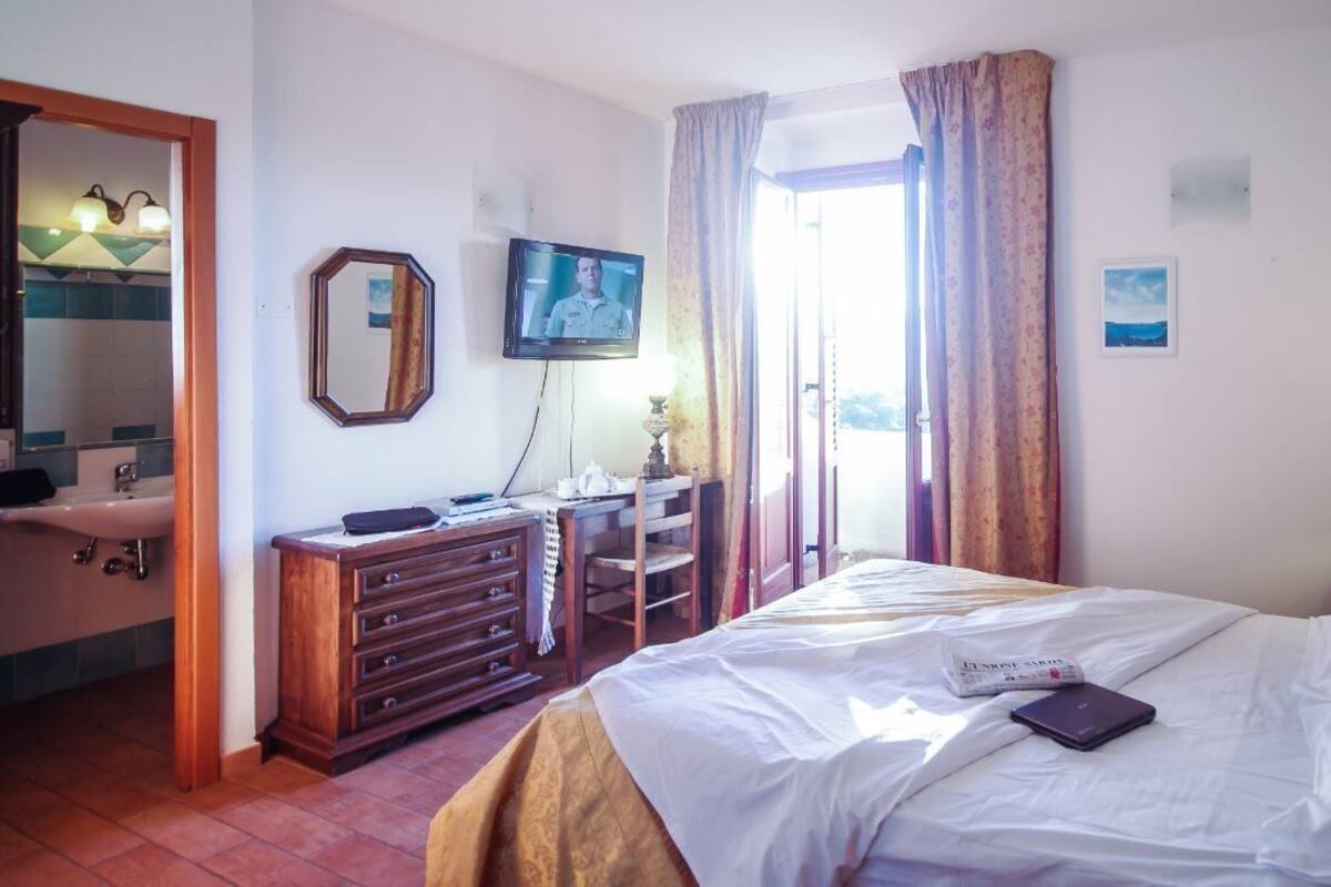 A hotel room with a bed, a desk with a computer, a television, a bathroom with a sink, and a window with curtains.