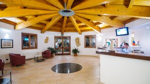 Zona de recepción con techo de madera, mostrador de recepción, televisor y área de estar con sillas y una mesa.