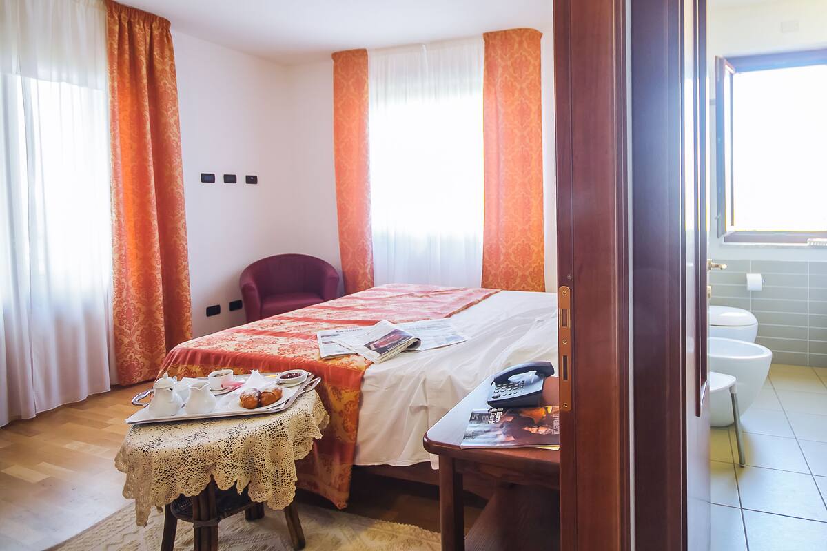 A hotel room with a bed, a table with breakfast items, a chair, a bathroom with a bathtub, toilet, and sink.