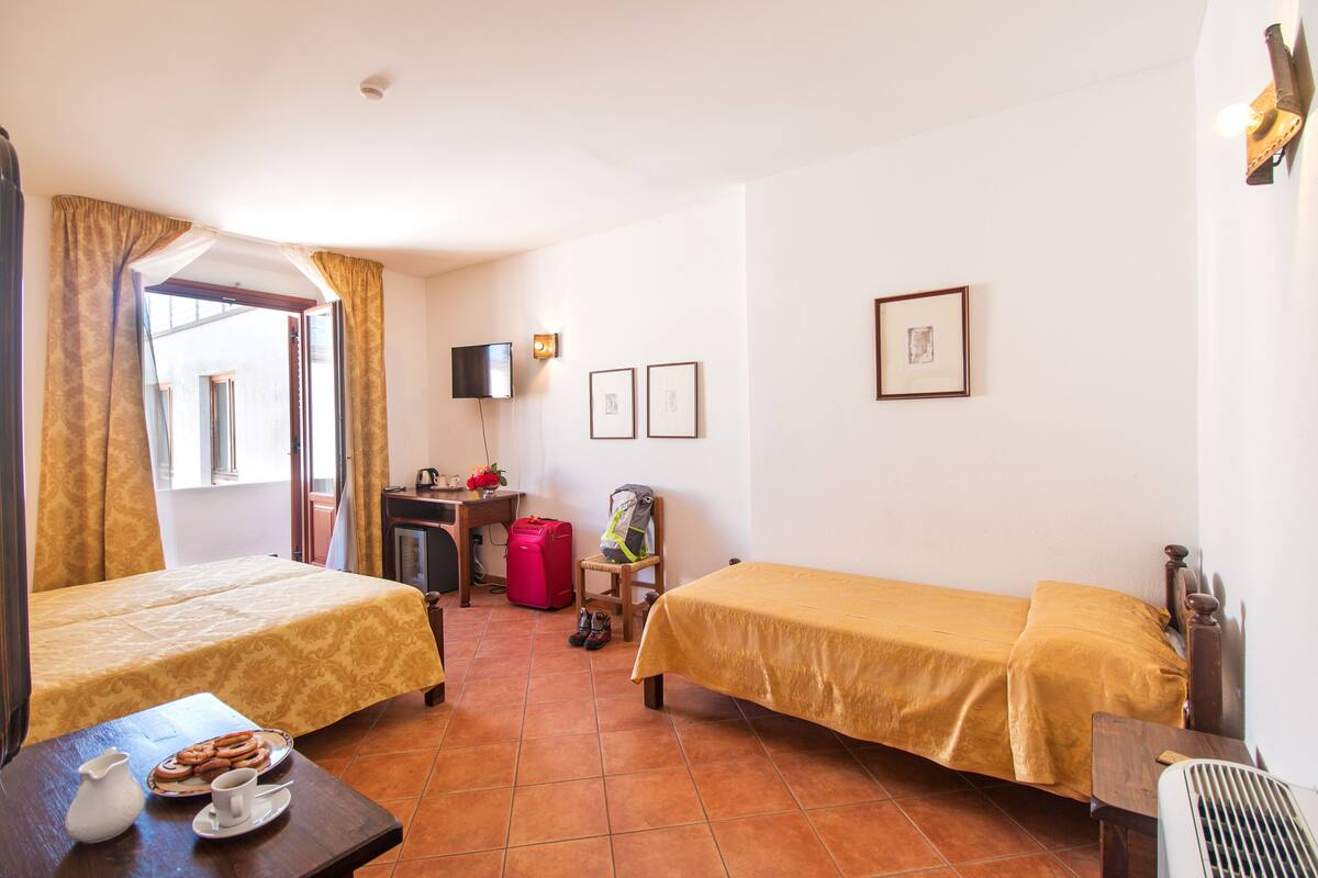 A hotel room with two beds, a desk, a chair, a table with breakfast items, and a window with curtains.