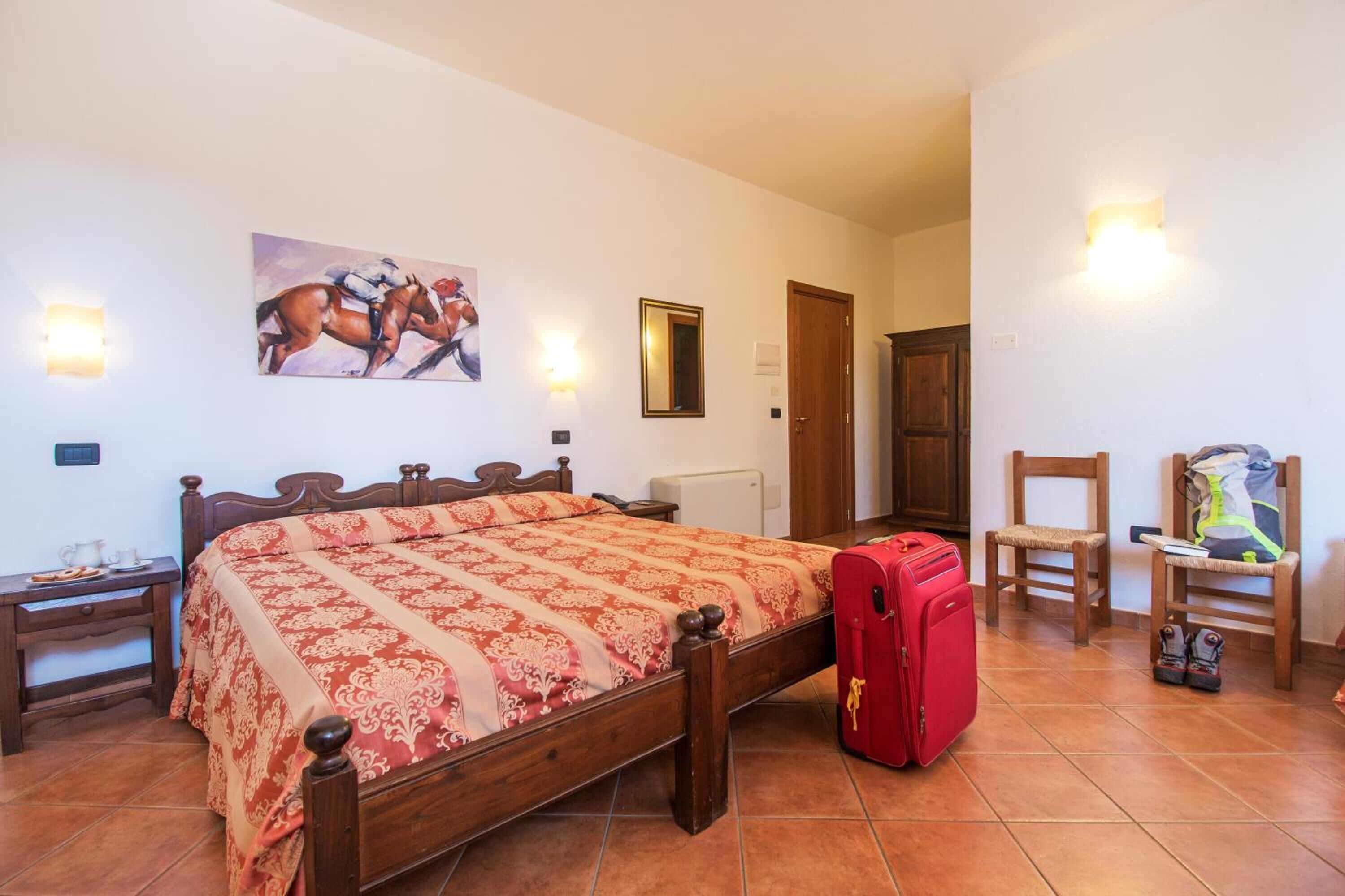 Quarto com cama de madeira, mala vermelha e cadeira com uma mochila.