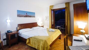 Una habitación de hotel con cama, mesita de noche con lámpara, una silla, televisor y ventana con cortinas.