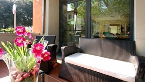 A wicker sofa on a patio with a glass door leading to a garden. - Hotel Montebello (Montecatini Terme)