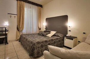 Una habitación de hotel con una cama grande, una mesita de noche con un teléfono, una silla y un escritorio.