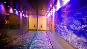 A hallway with glass walls, a blue textured wall, and emergency exit signs. - Hotel Montebello (Montecatini Terme)