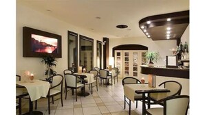 A dining area with tables and chairs, a television mounted on the wall, and a plant on the counter. - Hotel Montebello (Montecatini Terme)