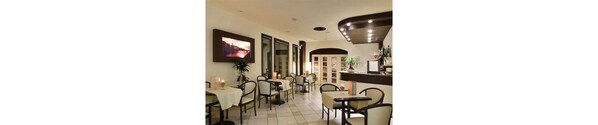 A dining area with tables and chairs, a television mounted on the wall, and a plant on the counter. - Hotel Montebello (Montecatini Terme)