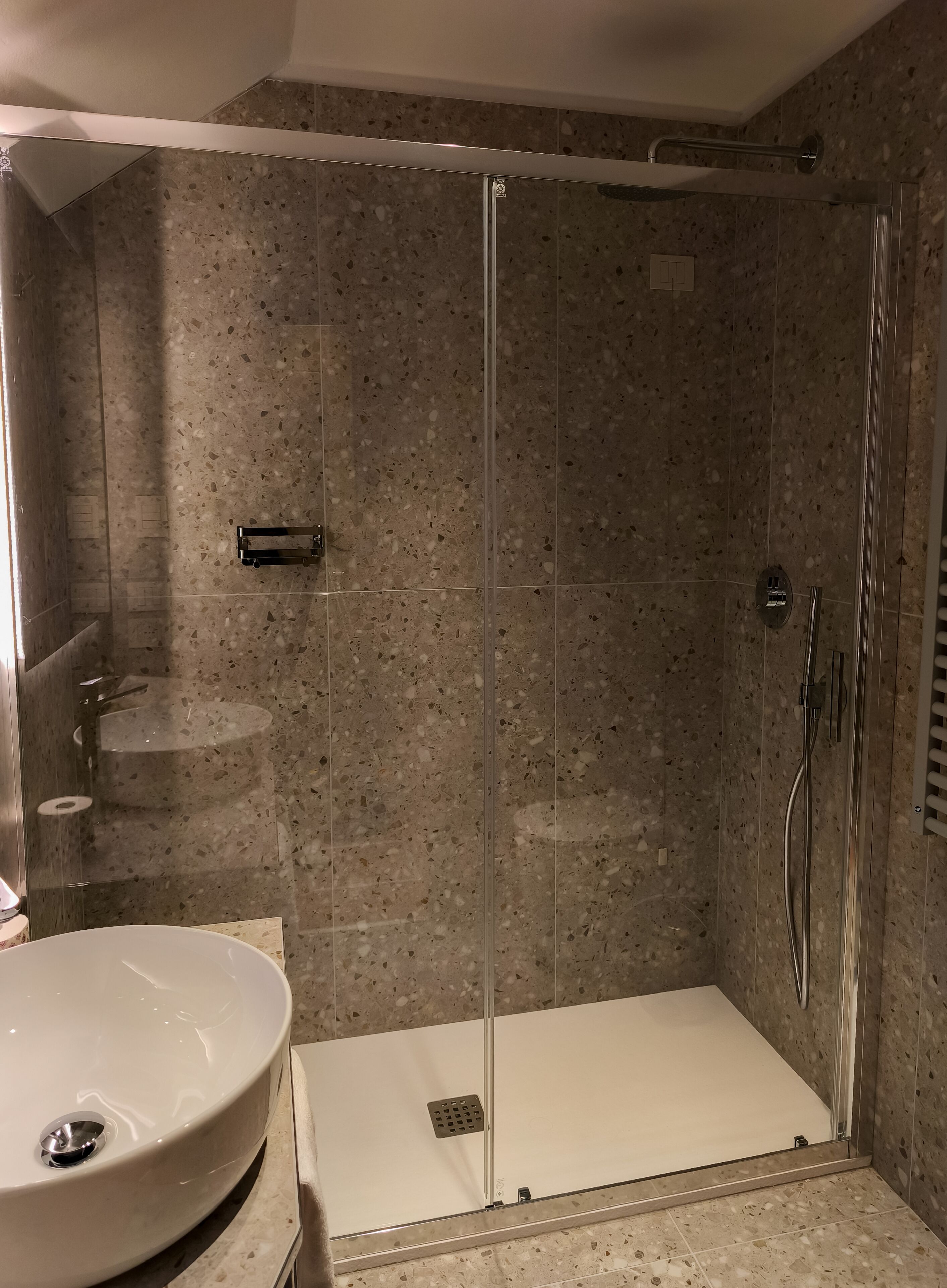 Eine Dusche ohne trittfeste Einstieg, mit Glastür, einem Waschbecken und einer Duschbrause.