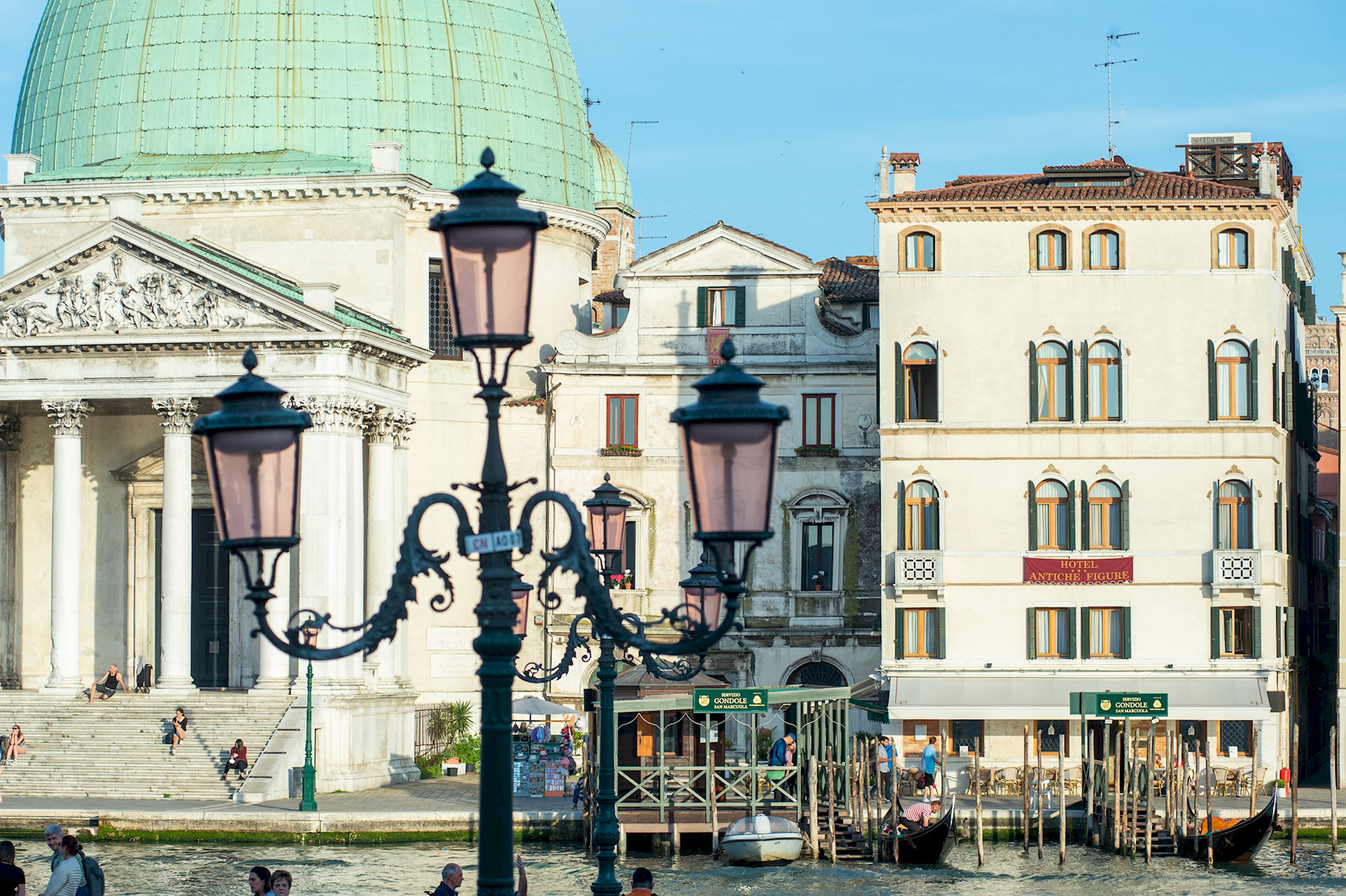 A historic building with a dome, a sign for Hotel Antico, and gondolas by the water.