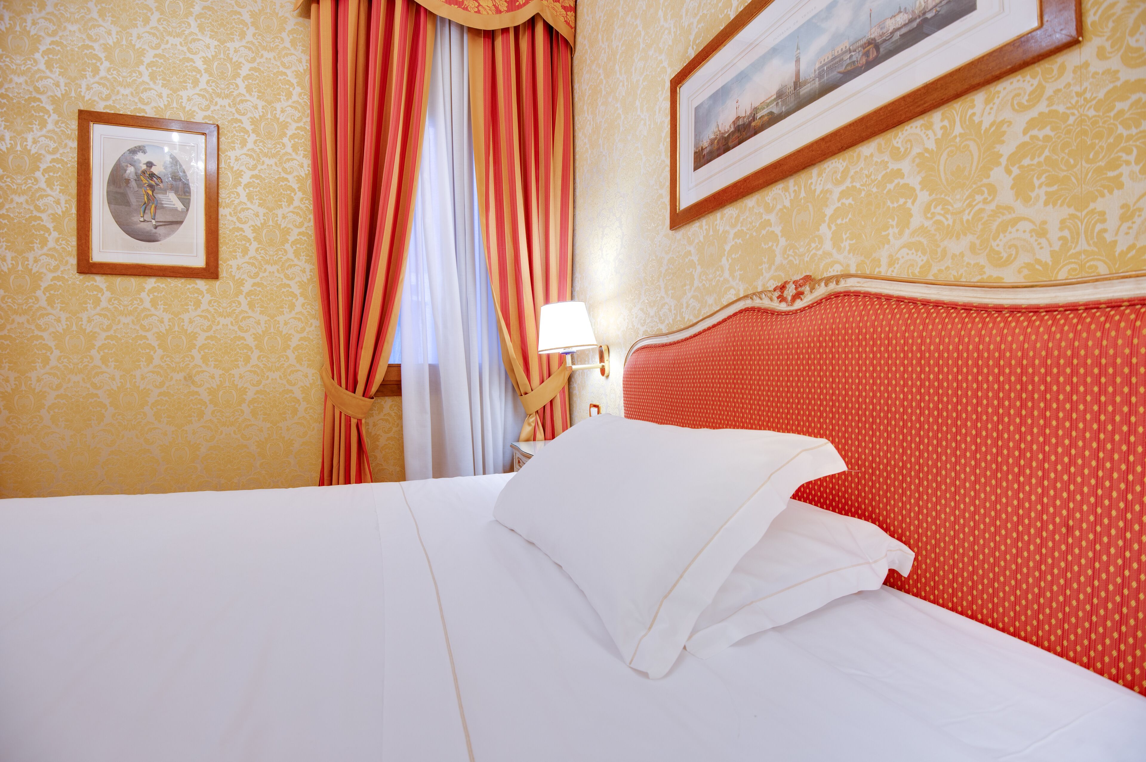 Una habitación de hotel con una cama grande, cortinas rojas, un cuadro en la pared y una lámpara en la mesita de noche.