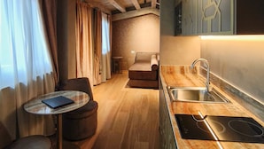 Une cuisine moderne dotée d’une cuisinière intégrée, un coin repas avec une table et des chaises, et un espace salon confortable avec un canapé et des rideaux.