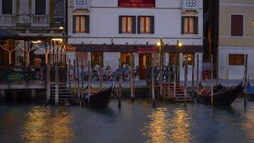 Un hotel sul lungomare con gondole ormeggiate nell'acqua, una terrazza con posti a sedere all'aperto e un cartello che recita "HOTEL ANTICHE FIGURE".