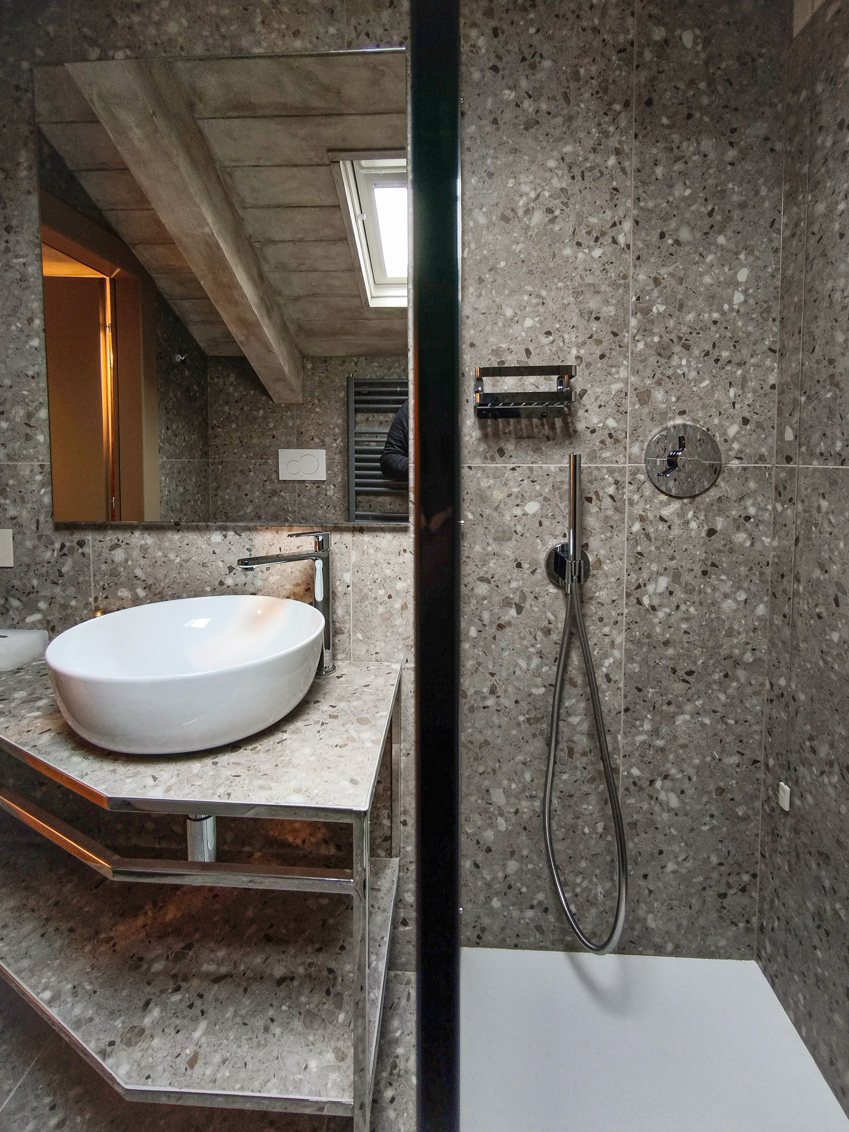 Un baño moderno con un lavamanos grande y blanco, una ducha con cabezal de ducha de mano y un espejo que refleja la habitación.