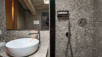 Un baño moderno con un lavamanos grande y blanco, una ducha con cabezal de ducha de mano y un espejo que refleja la habitación.