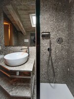 Un bagno moderno con un lavandino bianco di grandi dimensioni, una doccia con soffione manuale e uno specchio che riflette l'ambiente.